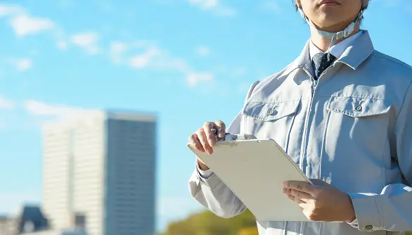 高層ビルを背景に、現場作業員が業務内容を記録しているイメージ