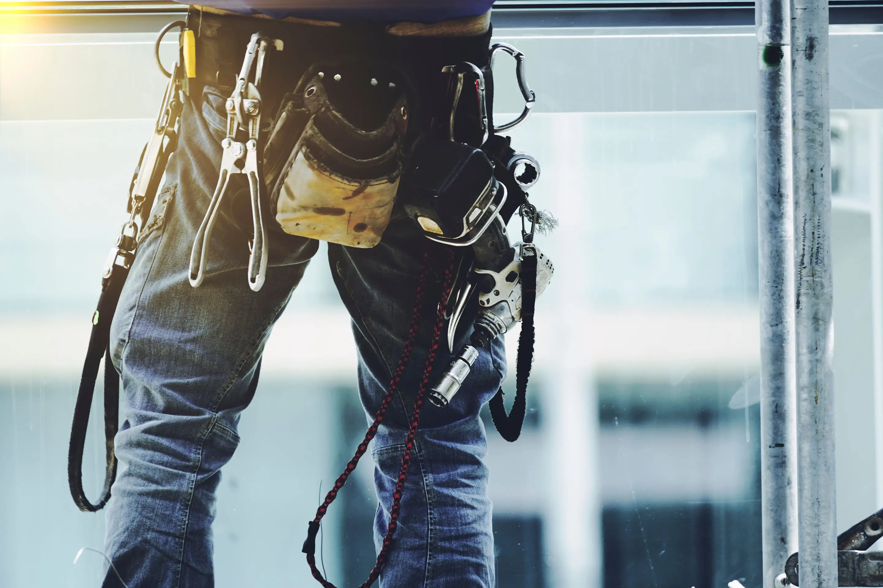 安全帯と工具を装着し、作業現場で立つ作業員の腰回りの様子