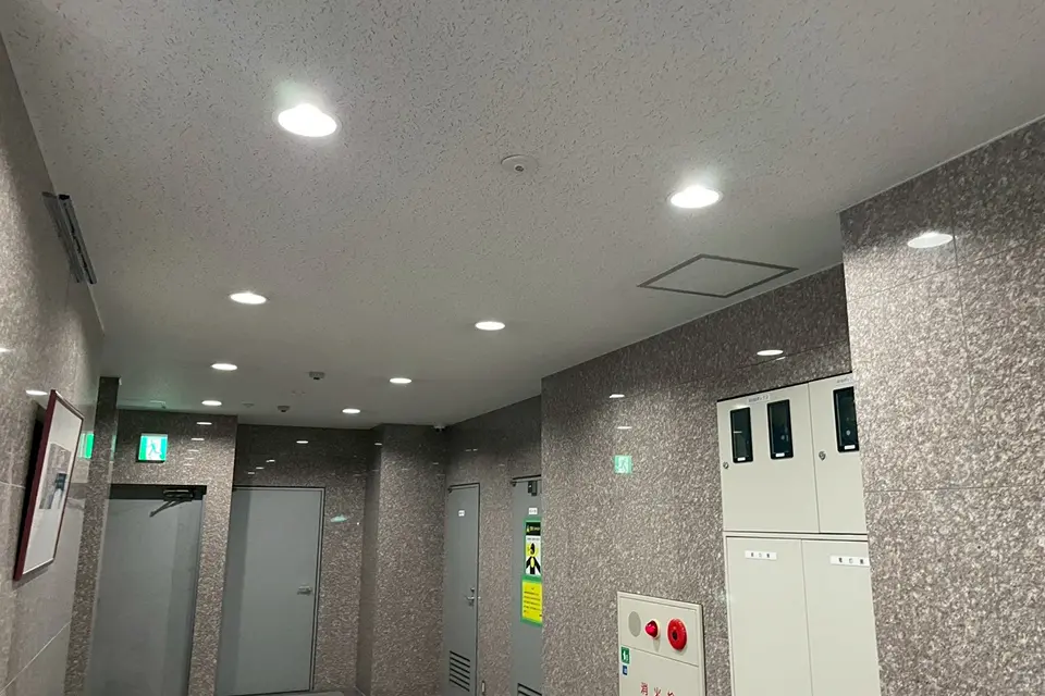 石目調の壁と設備盤が並ぶ、清潔感のあるオフィスビルの廊下